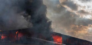 Firefighter on ladder spraying water at warehouse fire