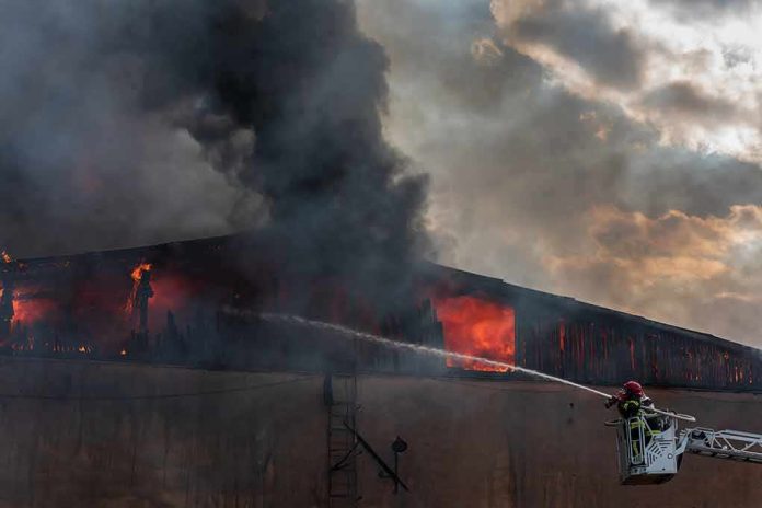 shutterstock_2362579223 Firefighter on ladder spraying water at warehouse fire