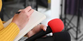 Journalist holding two microphones while writing in a notebook