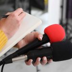 Trump Honors NASCAR Hero After Unexpected Death Journalist holding two microphones while writing in a notebook