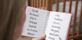 Hands holding a notebook with baby name lists near a crib