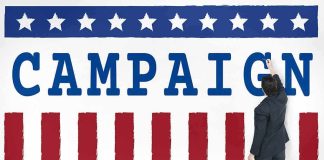 Man in suit writing on large campaign banner with stars and stripes