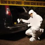 forensic investigator at car trunk behind crime scene tape