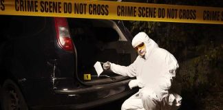 forensic investigator at car trunk behind crime scene tape