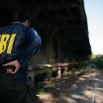 FBI agent stands under an overpass holding a radio