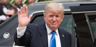 Donald Trump waves while standing beside a black vehicle