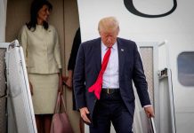 man in suit with red tie walking down airplane stairs