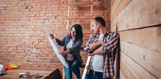 Two people reviewing blueprints in a rustic room under renovation
