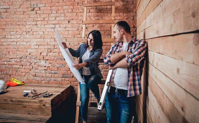 Two people reviewing blueprints in a rustic room under renovation