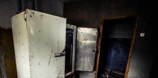 Abandoned room with open, rusted refrigerators and a dark doorway