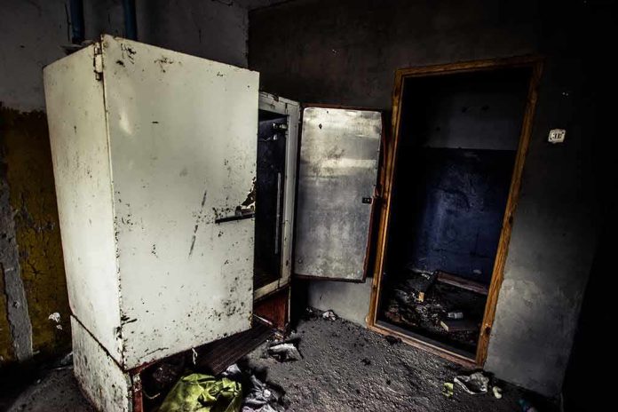 Abandoned room with open, rusted refrigerators and a dark doorway