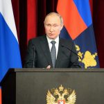 Vladimir Putin speaking at a podium with microphones