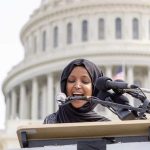 Woman in hijab speaking at podium with microphones
