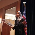 FBI Seize Omars Passport and Phone! Ilhan Omar speaking at a podium with a microphone