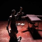 Lady Justice statue with scales in dramatic light beside an empty gurney