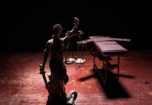 Lady Justice statue with scales in dramatic light beside an empty gurney