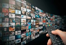 Hand holding remote control facing a wall of streaming thumbnails