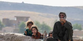 group of children and an older man sitting on a low wall outdoors