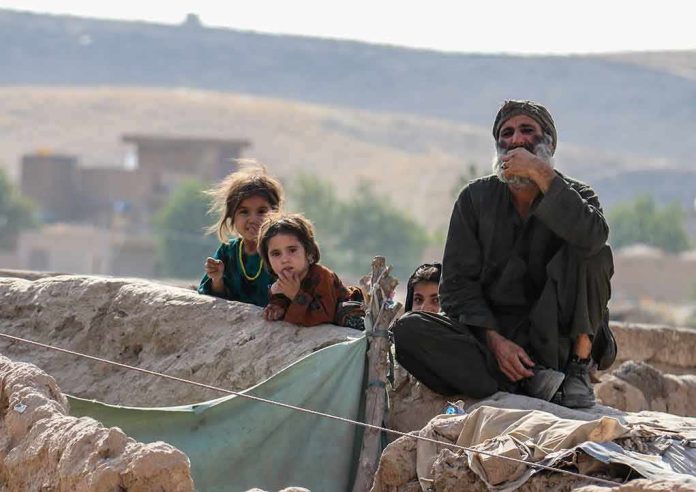 group of children and an older man sitting on a low wall outdoors