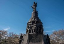 Bronze monument with allegorical figures under a clear blue sky