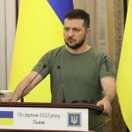 German Chancellor Meets Zelenskyy Amid Looming Russian Attacks Man at a podium with Ukrainian flags