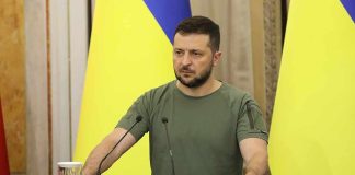 German Chancellor Meets Zelenskyy Amid Looming Russian Attacks Man at a podium with Ukrainian flags
