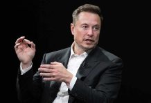 Elon Musk speaking in a black suit against a dark background