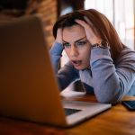 Woman frustrated at laptop, holding her head.