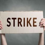 Two hands holding a cardboard sign saying strike