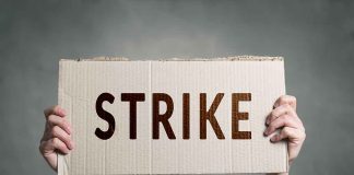 Two hands holding a cardboard sign saying strike