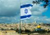 Israeli flag waving over Jerusalem city skyline.