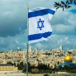 Israeli flag waving over Jerusalem city skyline.