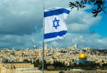 Israeli flag waving over Jerusalem city skyline.