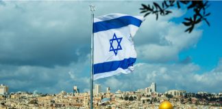 Israeli flag waving over Jerusalem city skyline.