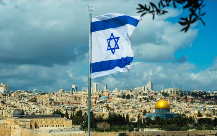 Israeli flag waving over Jerusalem city skyline.