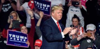 Man clapping at a rally with audience cheering.