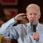 Man speaking into microphone, saluting gesture.