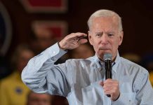 Man speaking into microphone, saluting gesture.