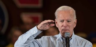 Man speaking into microphone, saluting gesture.