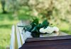 White roses on a polished wooden casket outdoors.