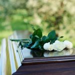 White roses on a polished wooden casket outdoors.