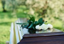 White roses on a polished wooden casket outdoors.