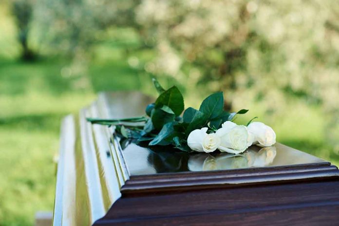 White roses on a polished wooden casket outdoors.