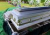 White coffin at a cemetery with flowers nearby.