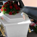 White coffin with red roses inside a hearse.