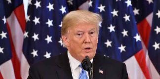 Man speaking at podium with American flags behind