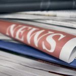 Stack of newspapers with "NEWS" headline visible.