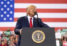 Man speaks at podium with U.S. flag background.