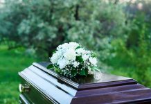 Coffin with white flowers outdoors in green surroundings.