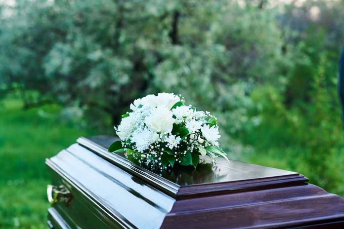 Coffin with white flowers outdoors in green surroundings.